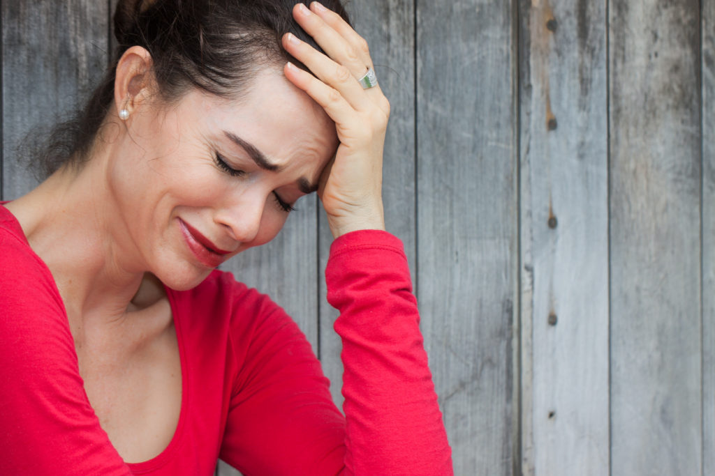 A woman in red shirt holding her head with one hand.