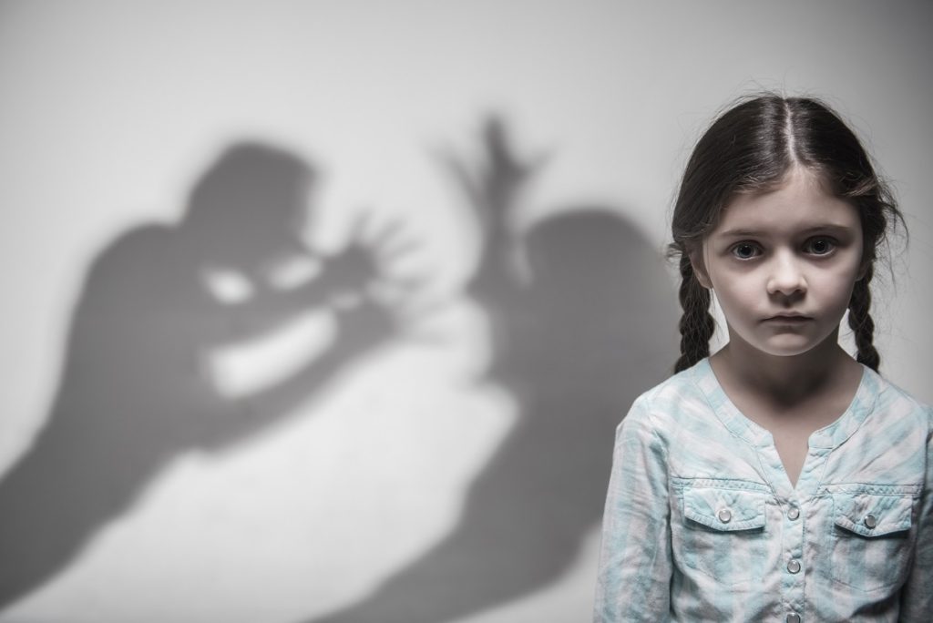 A girl standing in front of a wall with her shadow on the wall.